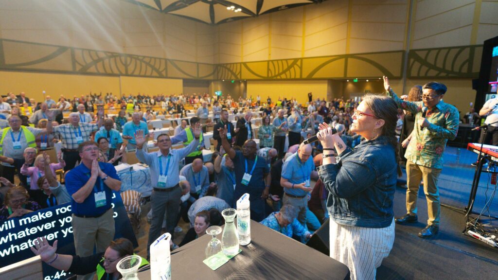 Worshipers in a conference meeting room sing and pray.