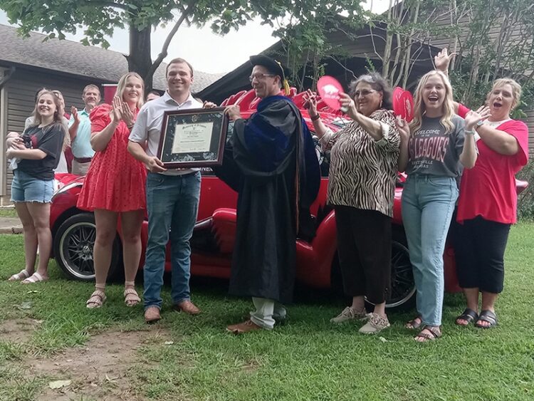 Tyler Huggins, center left, accepts his diploma from Kerry Melton of the College of Engineering while his wife, Anna, to his right, celebrates with other family members in Bono on June 26.