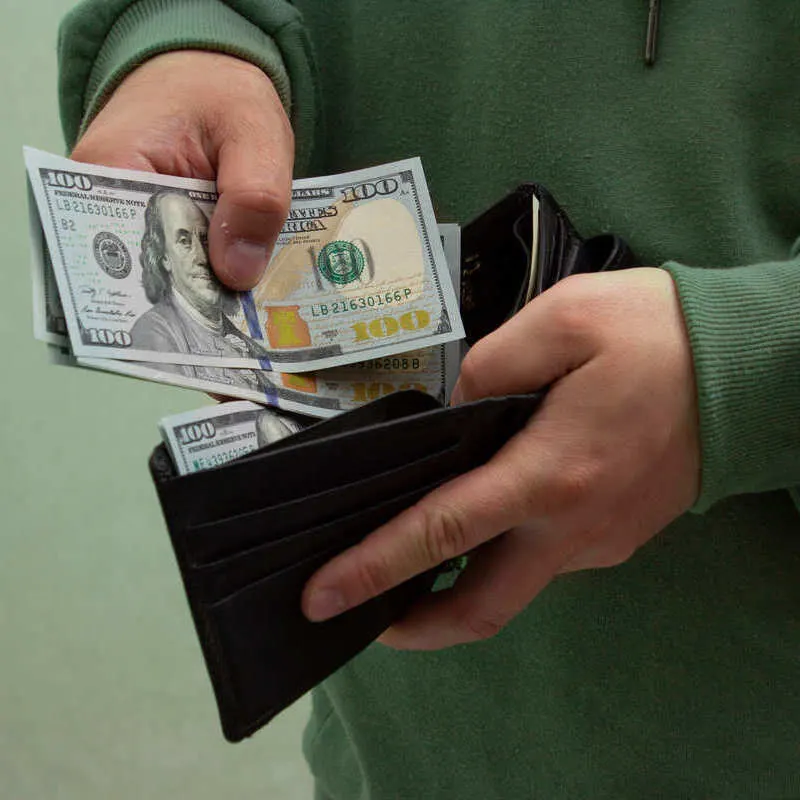 A Man Wearing A Green Hoodie As He Puts Dollars Away In His Wallet