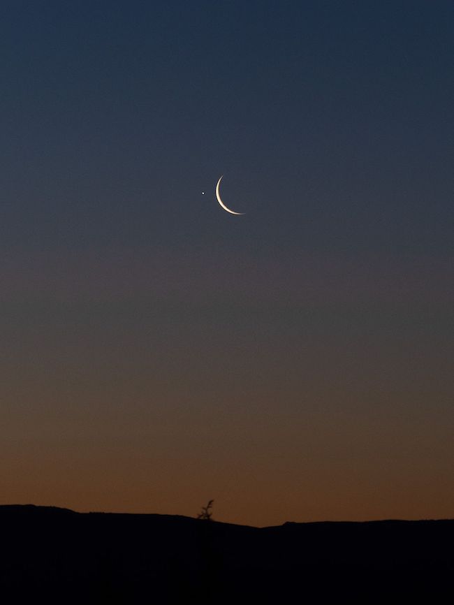 Jupiter near waning crescent moon with a dark horizon in the foreground.