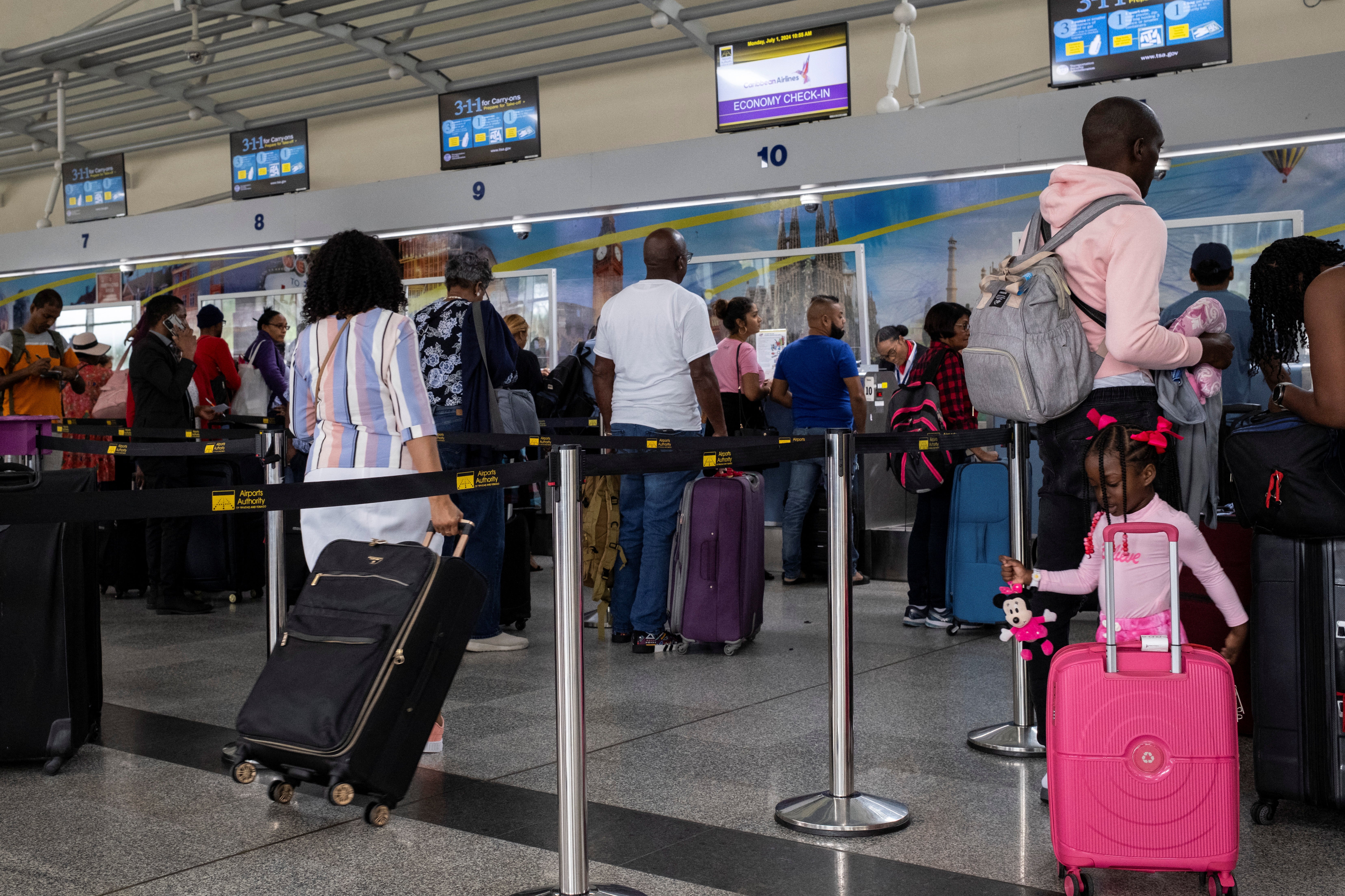 People line up at a counter in the Piarco international Airport as flights are canceled because of Hurricane Beryl