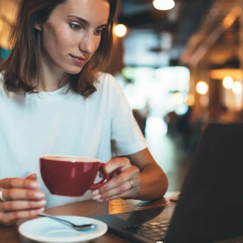 Young Woman Drinking Coffee As She Works From A Cafe