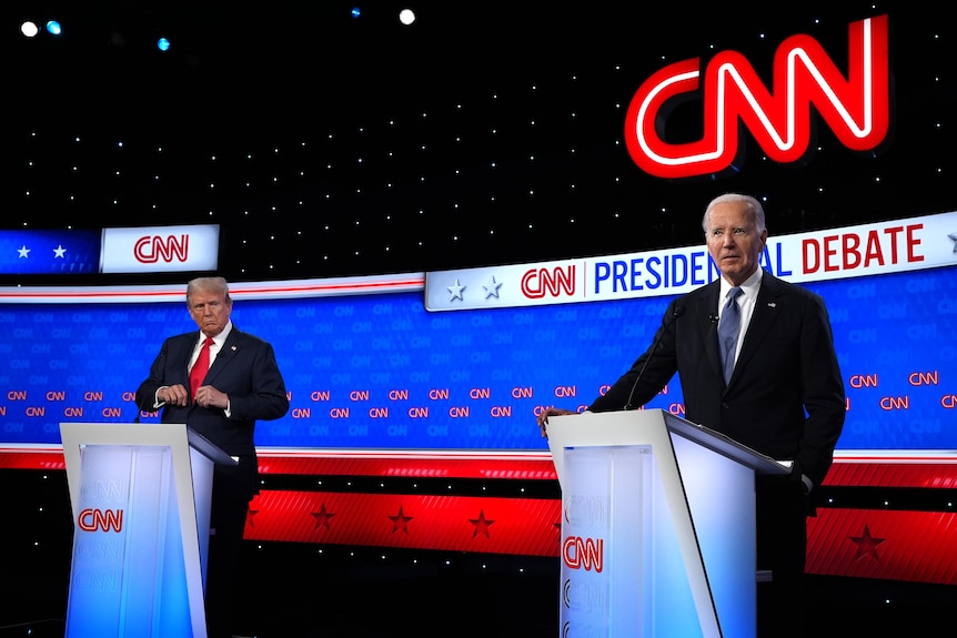 Two men in suits stand behind lecterns in front of 