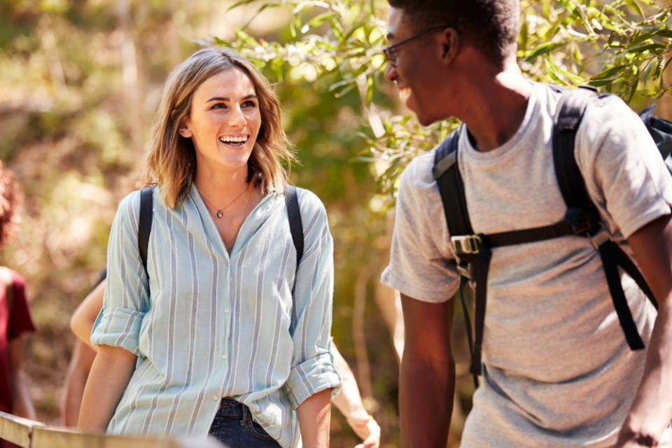 Happy interracial millennial couple hiking in a forest together, waist up.