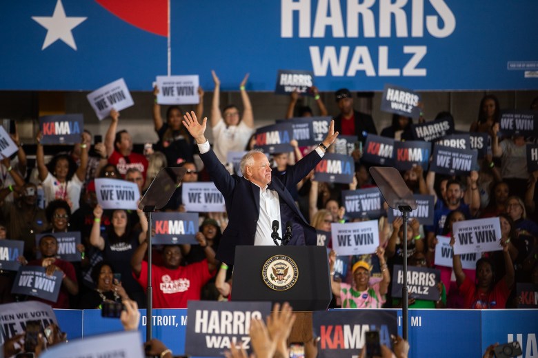 Minnesota Gov. Tim Walz raises his hands in the are while standing behind a podium during a presidential campaign rally.