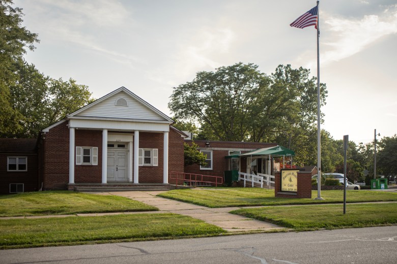 A brick building with columns at the front and American flag in the front yard serves as the American Muslim Center in Dearborn, Michigan.