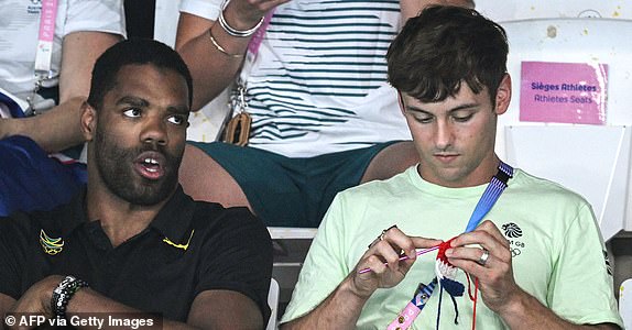 Britain's Tom Daley knits in the stands next to Jamaica's Yona Knight-Wisdom during the women's 3m springboard diving final during the Paris 2024 Olympic Games at the Aquatics Centre in Saint-Denis, north of Paris, on August 9, 2024. (Photo by Oli SCARFF / AFP) (Photo by OLI SCARFF/AFP via Getty Images)