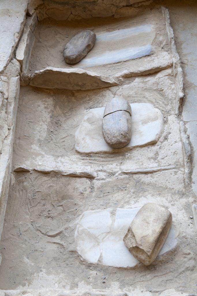 Three corn grinding stones laid against flat surfaces on a sandy ground