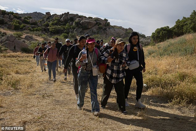 Migrants from South and Central America hold hands as they stride towards a gap in the border wall before crossing into Boulevard, California from Tecate, Mexico, May 20, 2024