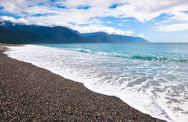 taiwan beaches foamy waves rolling in on gravel sand with mountains in the background