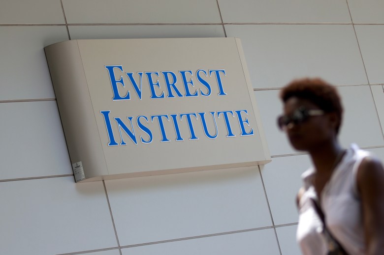 A person wearing sunglasses and a white sleeveless shirt walks past a sign that reads, Everest Institute.