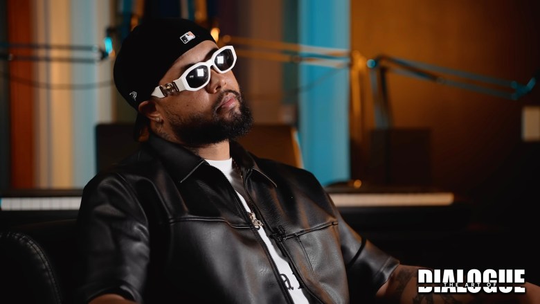 A person in white sunglasses and a black leather jacket sits in a room during an interview.