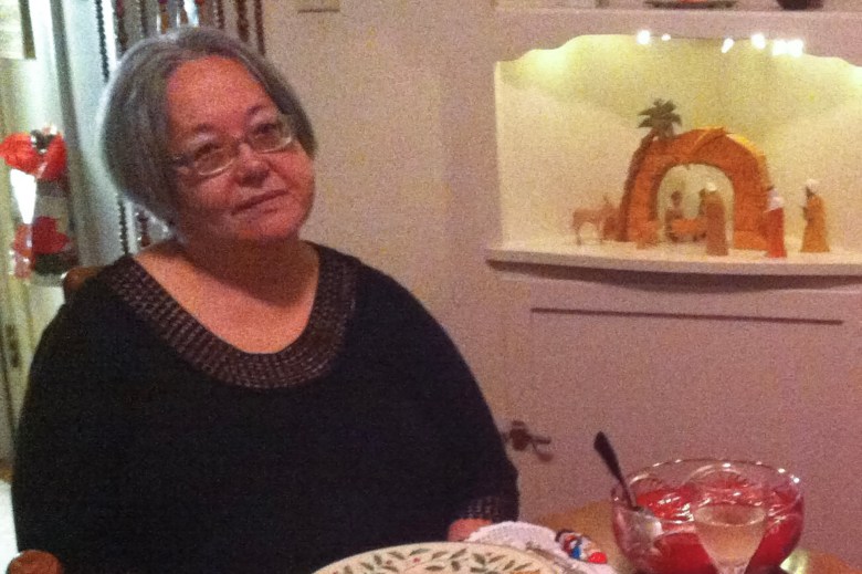 A person wearing a black shirt sits at table, next to a punch bowl, while a nativity scene sits on a mantle.