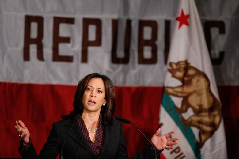 Former California Attorney General Kamala Harris, wearing a black blazer with a maroon pattern shirt and standing behind a giant California state flag, gives her first news conference in Los Angeles on Nov. 30, 2010. Photo by Damian Dovarganes, AP Photo