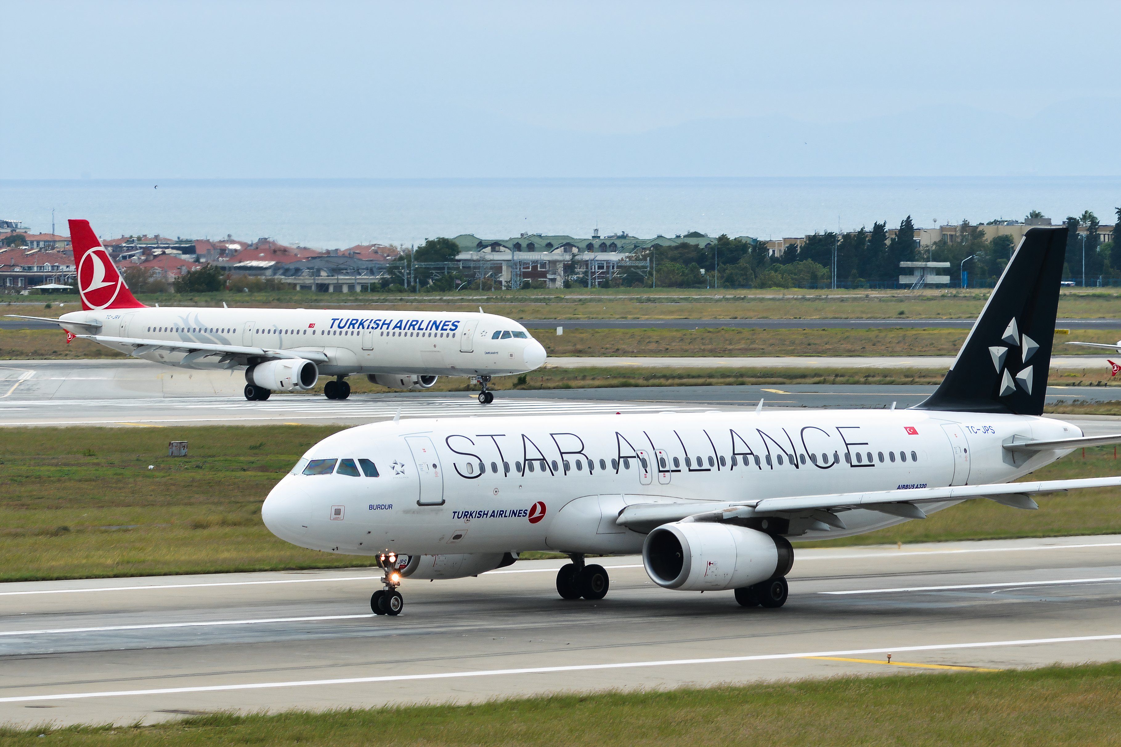 TC-JPS Turkish Airlines Airbus A320 (Star Alliance Livery) taxiing on runway of Istanbul Ataturk Airport (IST) alongside a plane in the traditional livery