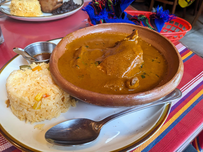 A plate with yellow rice and a bowl of curry, accompanied by a spoon, on a colorful table.