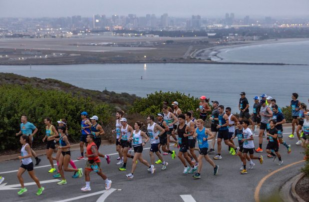 SAN DIEGO, CA - AUGUST 18, 2024: With San Diego Bay and the downtown San Diego skyline in the background, half marathon runners run toward the start line at Cabrillo National Monument during the 47th annual America's Finest City Half Marathon and 5K in San Diego on Sunday, August 18, 2024. Over 1,300 people participated in the 5K and more than 4,300 in the half marathon. (Hayne Palmour IV / For The San Diego Union-Tribune)