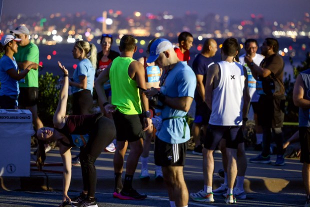 With an early morning view of the downtown San Diego skyline in the background, half marathon runners stand and stretch before a 6:15 am start time at Cabrillo National Monument during the 47th annual America's Finest City Half Marathon and 5K in San Diego on Sunday, Aug. 18, 2024. Over 1,300 people participated in the 5K and more than 4,300 in the half marathon. (Hayne Palmour IV / For The San Diego Union-Tribune)