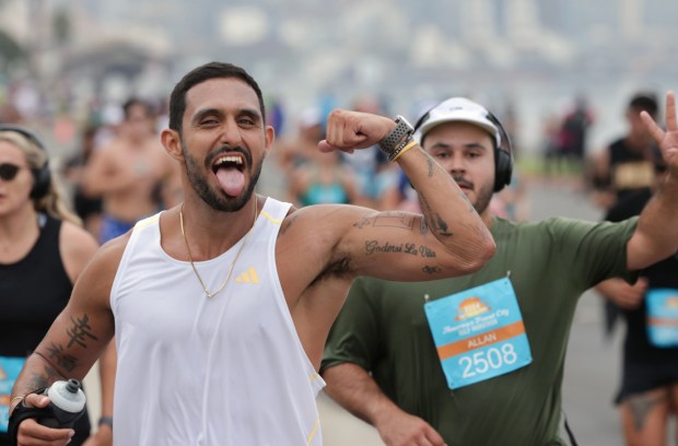 A pair of runners perform for the camera as they and thousands of people participating in the half marathon run on Harbor Island Drive during the 47th annual America's Finest City Half Marathon and 5K in San Diego on Sunday, Aug. 18, 2024. Over 1,300 people participated in the 5K and more than 4,300 in the half marathon. (Hayne Palmour IV / For The San Diego Union-Tribune)