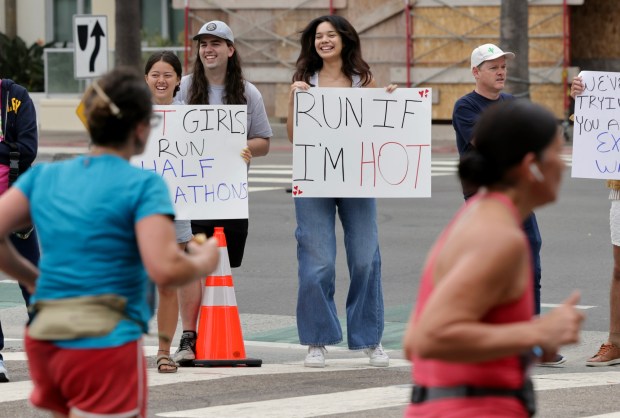 People hold signs as they cheer on half marathon runners after the runners turned on to West Ash Street from North Harbour Drive during the 47th annual America's Finest City Half Marathon and 5K in San Diego on Sunday, Aug. 18, 2024. Over 1,300 people participated in the 5K and more than 4,300 in the half marathon. (Hayne Palmour IV / For The San Diego Union-Tribune)