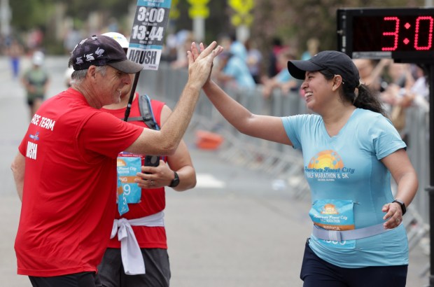 Half marathon runners Jessica Alvarez and Kevin Hopp high five as they cross the finish line in Balboa Park during the 47th annual America's Finest City Half Marathon and 5K in San Diego on Sunday, Aug. 18, 2024. Over 1,300 people participated in the 5K and more than 4,300 in the half marathon. (Hayne Palmour IV / For The San Diego Union-Tribune)