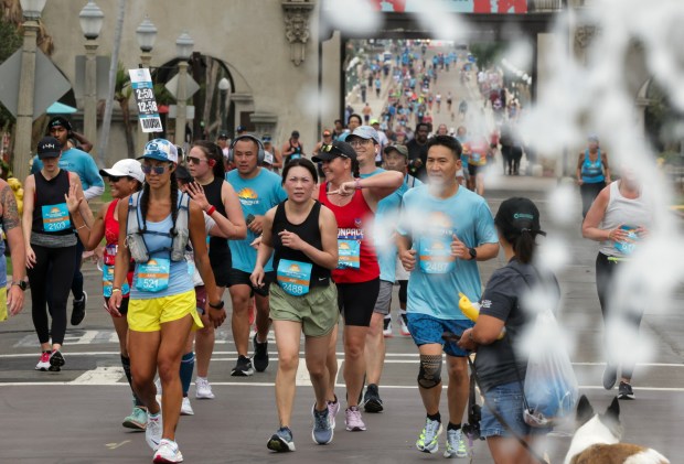 With the Plaza de Panama fountain splashing in the foreground, half marathon runners near the finish line in Balboa Park during the 47th annual America's Finest City Half Marathon and 5K in San Diego on Sunday, Aug. 18, 2024. Over 1,300 people participated in the 5K and more than 4,300 in the half marathon. (Hayne Palmour IV / For The San Diego Union-Tribune)