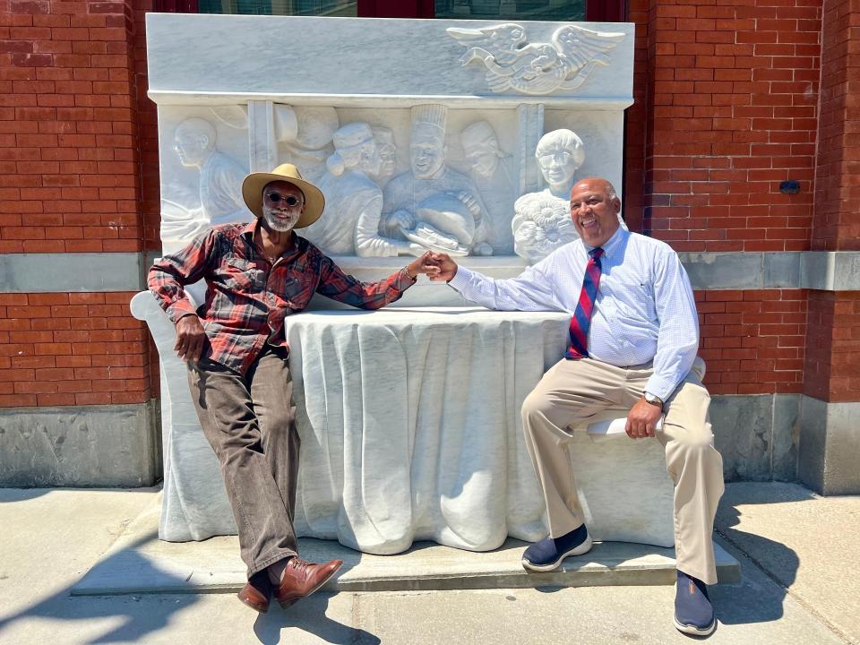 Al Wakefield, left, and Gerry Fernandez, right, pose at the Ernie and Willa Royal statue in Rutland, Vermont. The stone statue is an interactive piece in the town's downtown area honoring Ernie, the state's first Black restaurant owner.