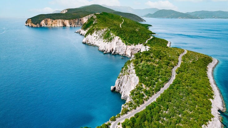 An aerial view of Lefkada Island, Greece, with a road cutting through the green plants and the peninsula surrounded by deep blue water. 