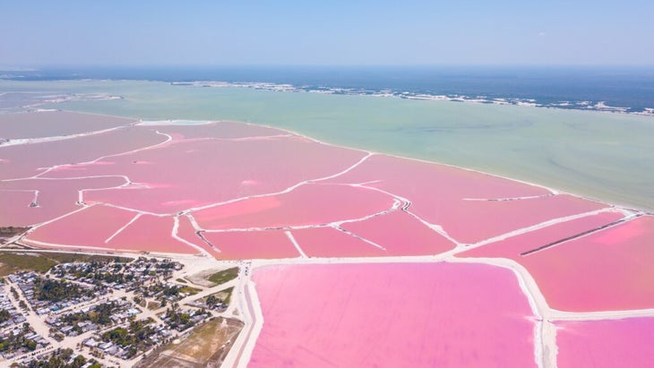 A lagoon divided by white sands into different hues of pink, with the turquoise waters of the Caribbean behind it.