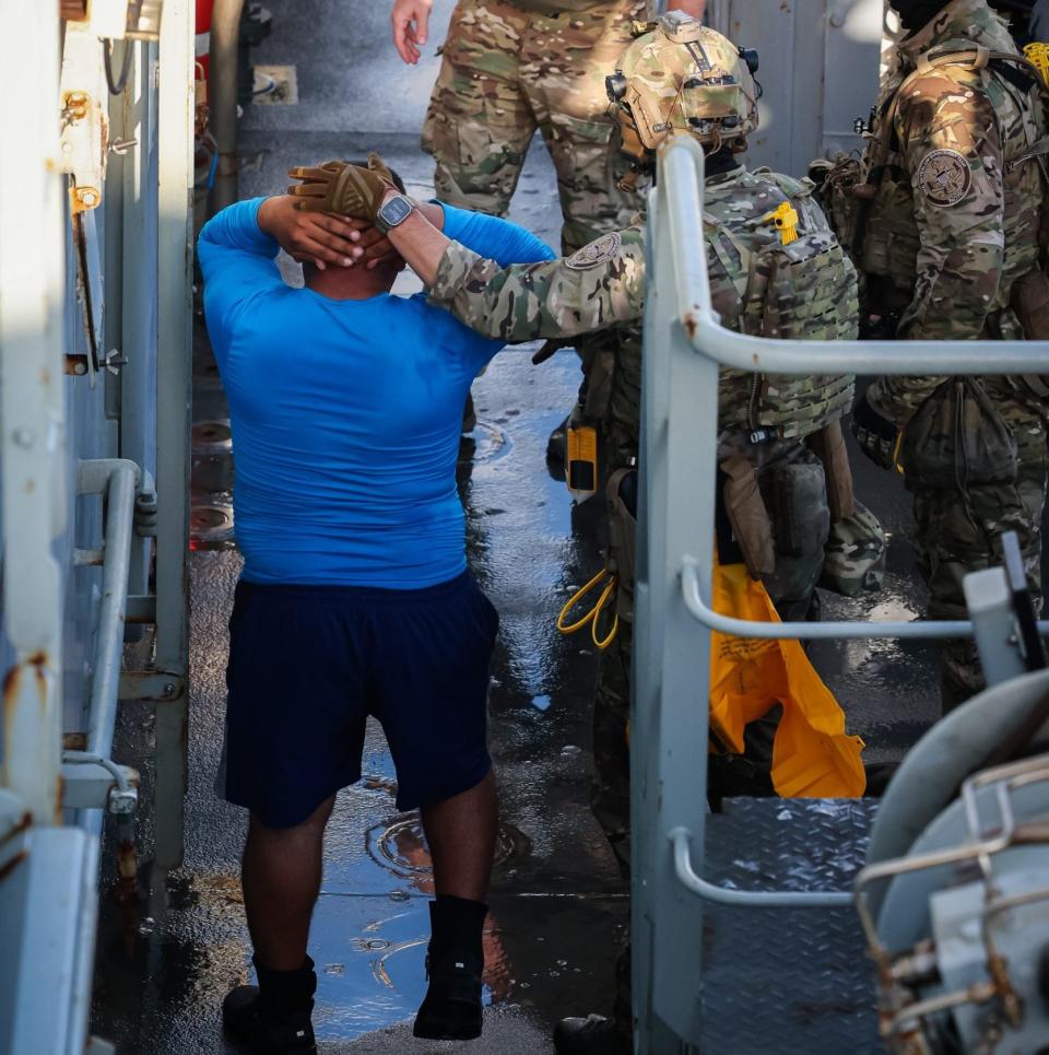 One of the alleged smugglers from the boat is taken on to HMS Trent with his hands above his head