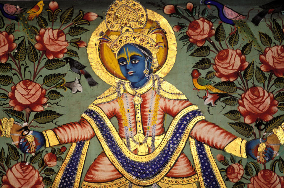 A traditional Indian painting depicts deity Krishna, adorned with intricate jewelry and surrounded by blossoming flowers and birds