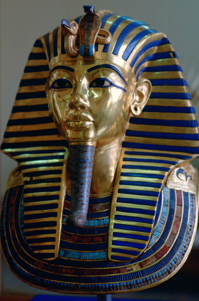 The image is of the famous gold mask of Tutankhamun, depicting the pharaoh wearing a headdress with a cobra symbol