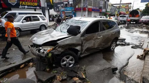 EPA A man walks next to a vehicle that was swept away by the current of rain in Santo Domingo, Dominican Republic, 19 November 2023.