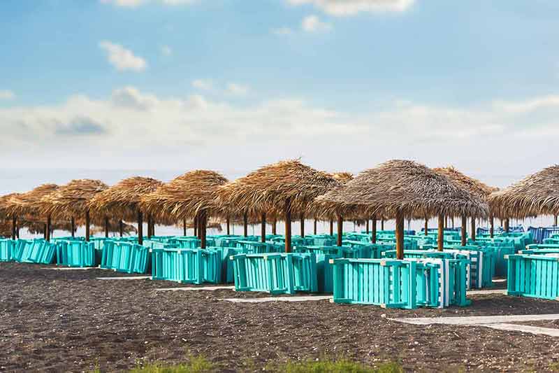 black sand beach greece thatched umbrellas on the beach
