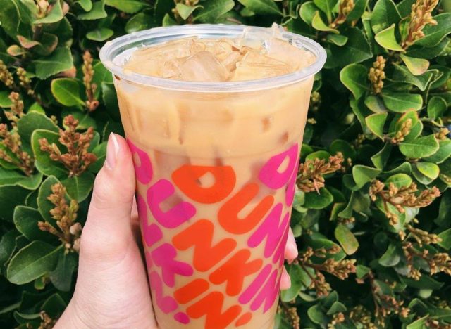 hand holding cup of Dunkin' iced coffee with green bush in the background