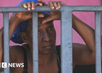 A man standing on the open back of a car looks back towards the camera