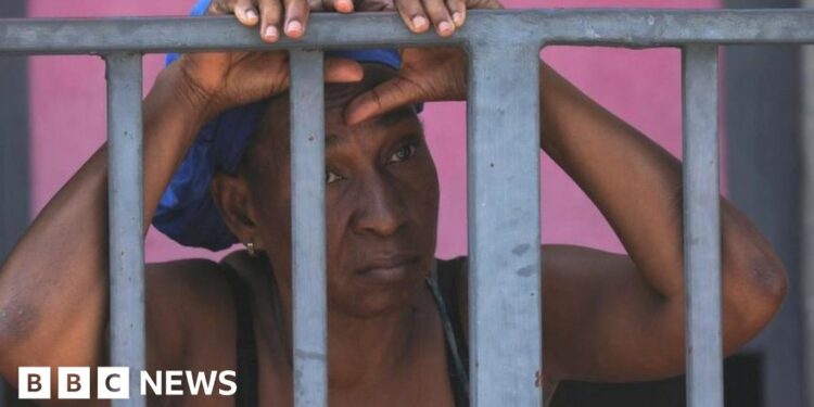 A man standing on the open back of a car looks back towards the camera