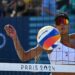 Brandie Wilkerson of Canada, with a white bikini top, black visor and mirrored sunglasses, eyes the ball through the net at the 2024 Olympic Beach Volleyball.