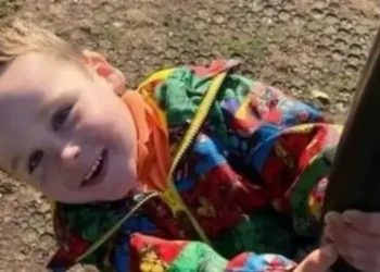 Family Young boy smiling in a multi-coloured jacket while holding a black pole