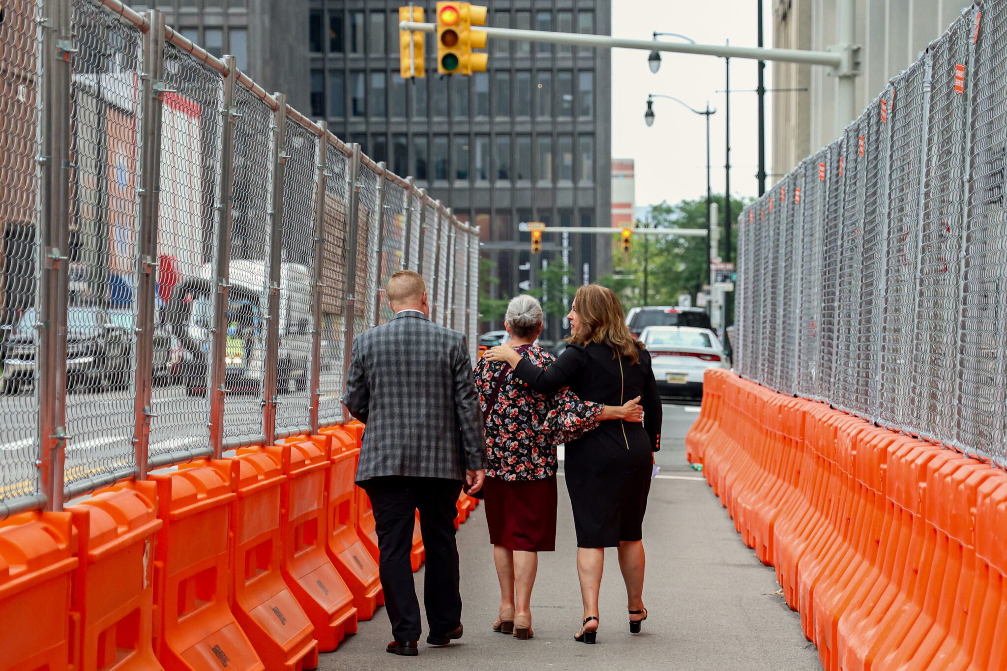 Two women and a man walk between rows of orange bollards on a city street under construction.