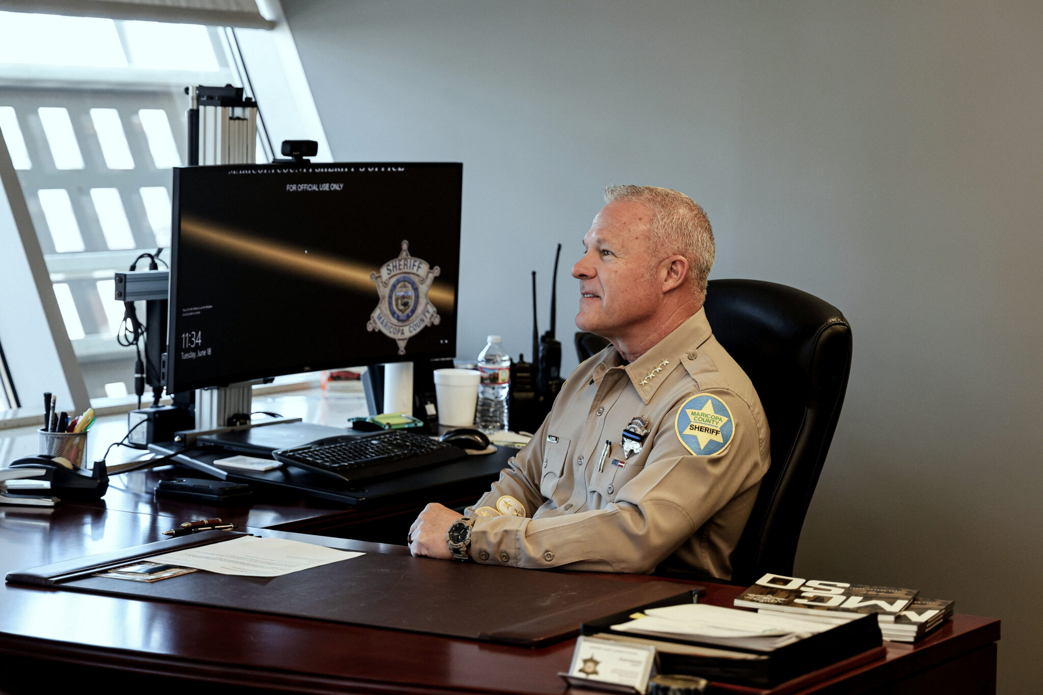 An older white man in a sheriff's uniform sits at a desktop computer.