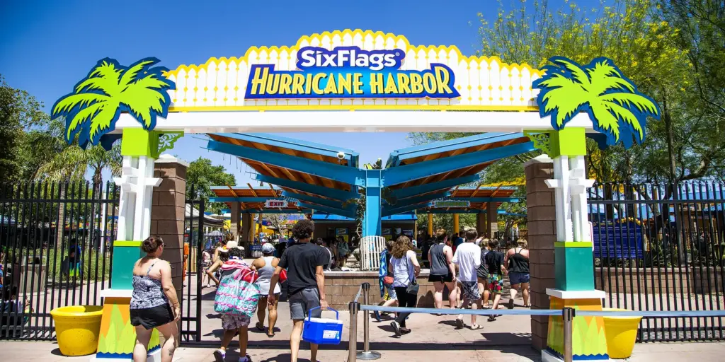 People entering Six Flags Hurricane Harbor water park under a colorful entrance sign with palm tree imagery.