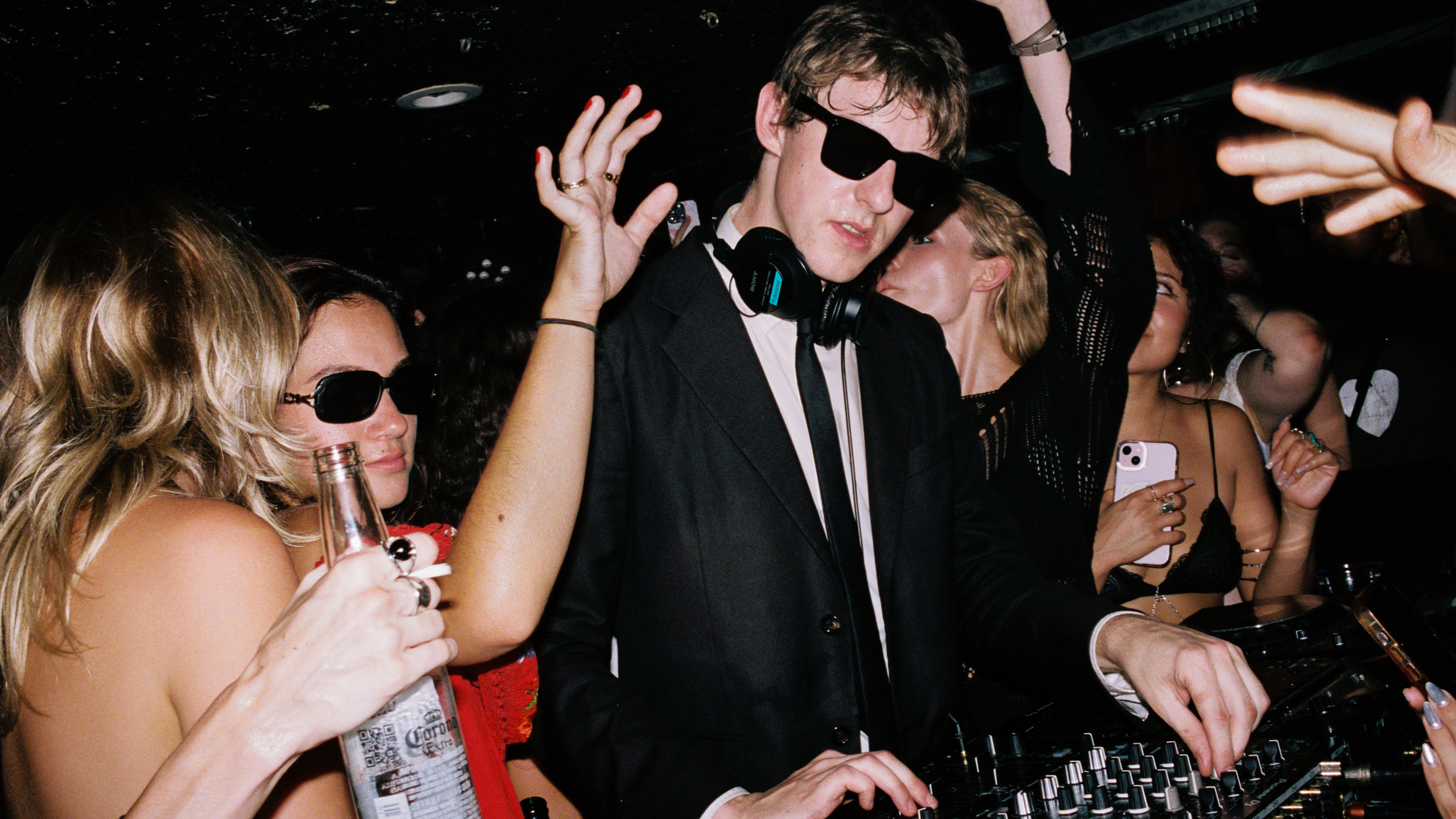 An image of The Dare wearing a suit and sunglasses while DJ-ing at a party