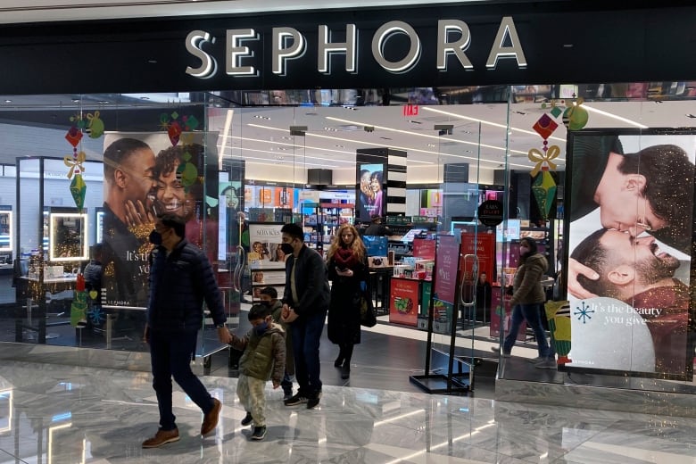 People walk out of and past a cosmetics store entrance into a ma.