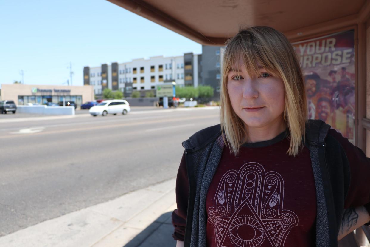 Phoenix resident Tiffany Sendelvach, 30, waits at the Indian School Road and 15th Avenue bus stop on July 22, 2024, as she heads to work. Sendelvach says long-sleeve sweaters and hoodies keep the sun off and help her feel cooler.