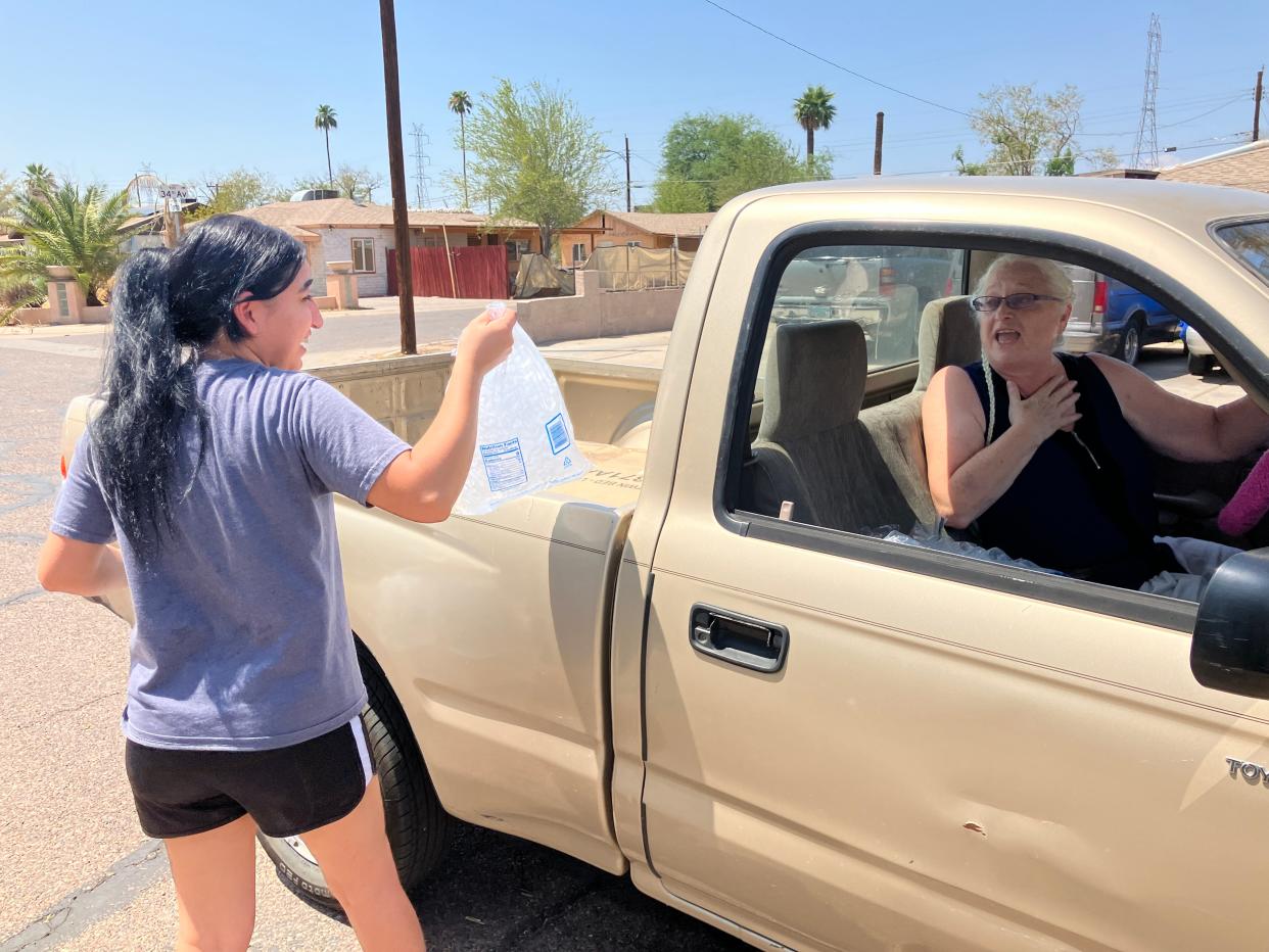 Paulina Alire grabs bags of ice that Chery Murillo picked up from APS and is distributing to neighbors without power on July 26, 2024. The neighbors near 35th Avenue and Broadway Road in Phoenix had been without electricity and air conditioning for two days after a storm downed APS power poles nearby.