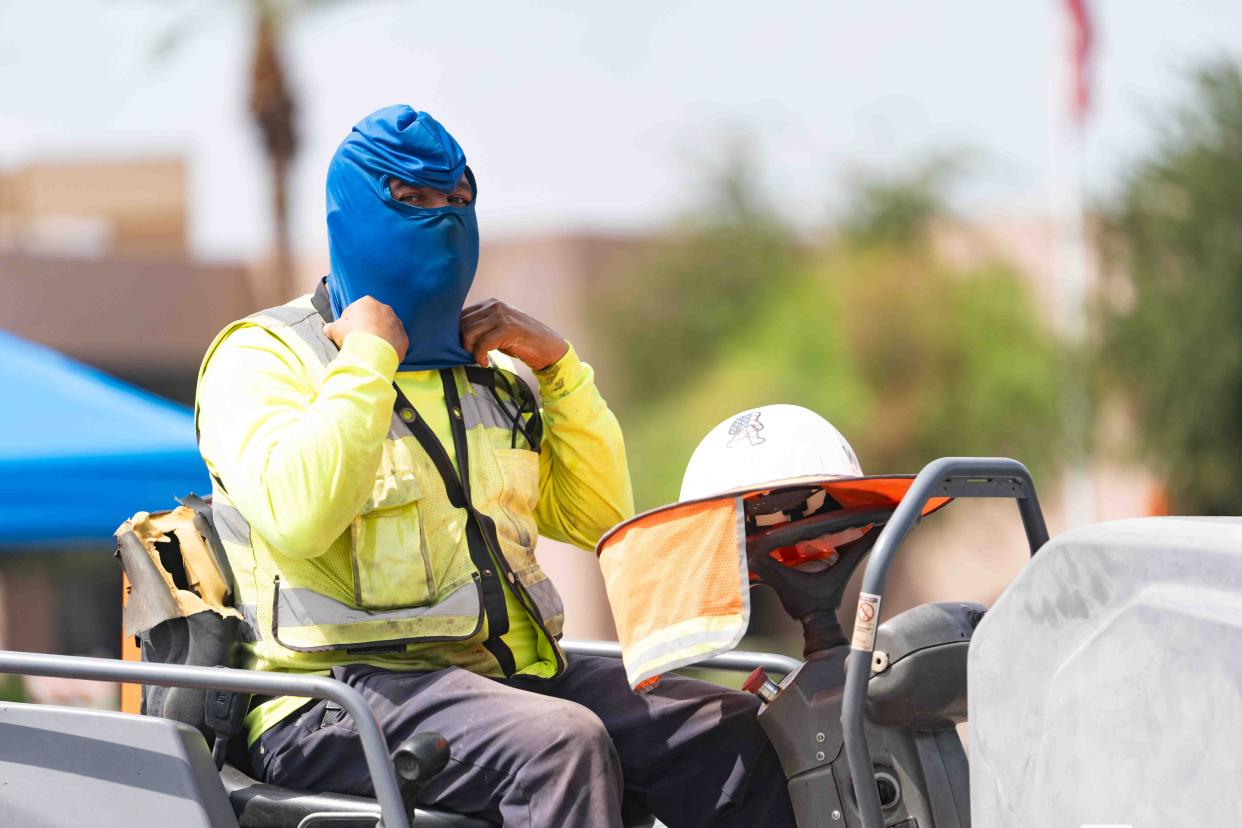 Ezekiel Lara covers his face to protect it from the sun as he lays asphalt at Desert Sky Mall in Phoenix on July 25, 2024.