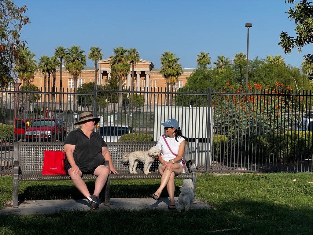 Amy Hurley (left) and Johnnie McDonald enjoy each other’s company at Hance Park Dog Park in Phoenix on July 28, 2024. They both regularly bring their dogs in the early morning before it gets too hot. Hurley sits on a cooling pack and stores chilled water in her insulated grocery bag.