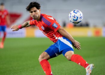 Victor Davila flicks the ball on the pitch, in his red shirt and blue shorts, ahead of the Chile vs Bolivia live stream.