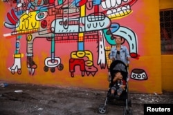 A woman stands by a mural titled 